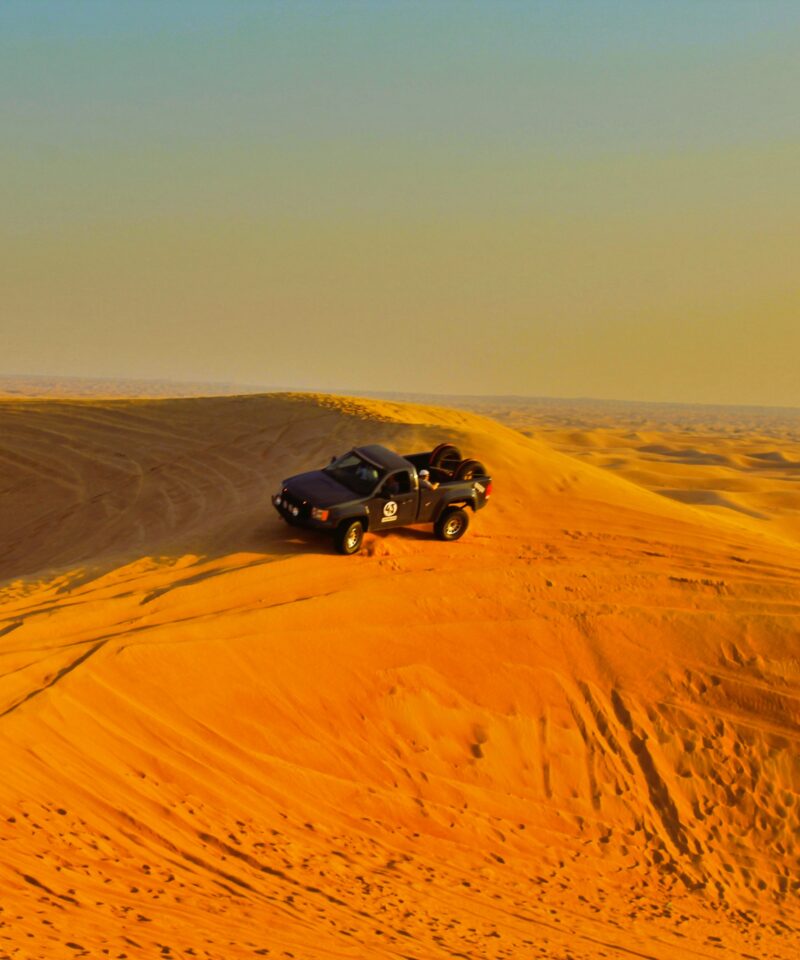 Abu Dhabi desert safari dunes with 4x4 vehicle at sunset