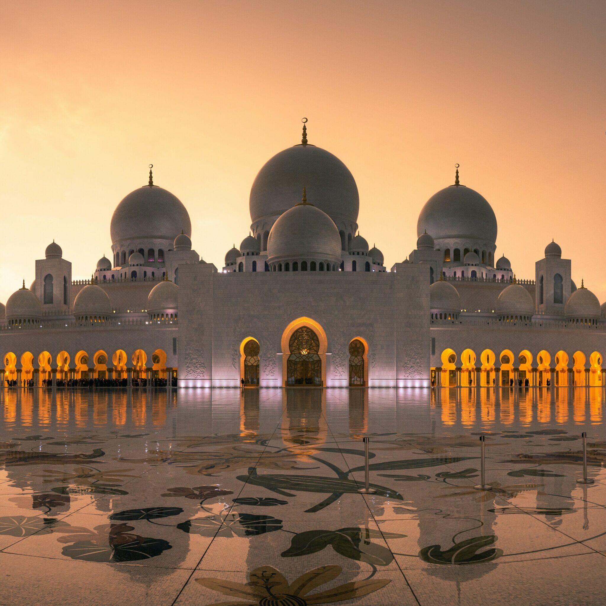 Sheikh Zayed Grand Mosque at sunset with illuminated arches and reflections